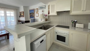 Une cuisine moderne avec des meubles blancs, un lave-vaisselle encastré, une cuisinière et un évier. Des tableaux encadrés ornent le mur, et une fenêtre est agrémentée de rideaux.