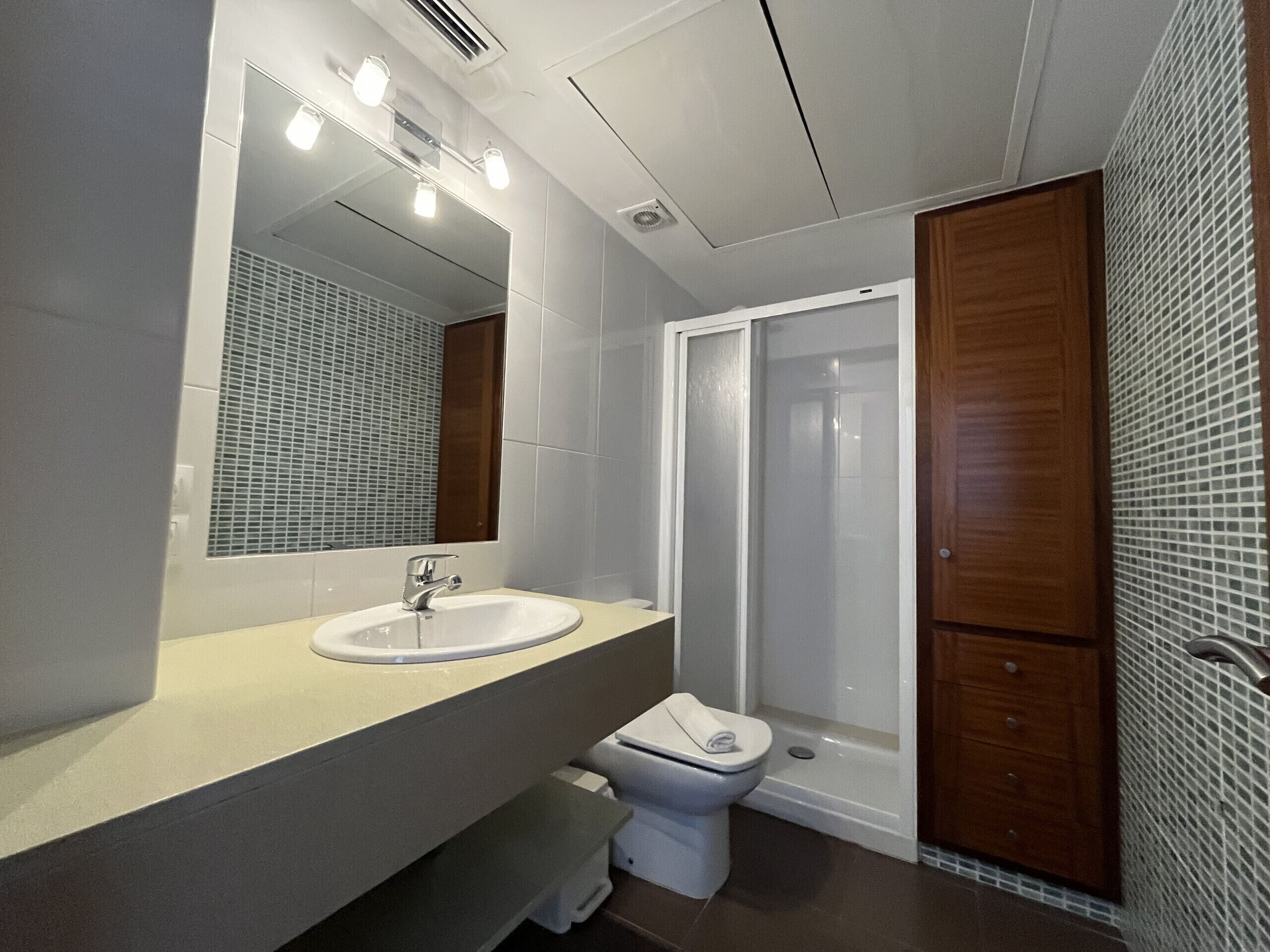 Een moderne badkamer met een wit wastafelmeubel, spiegel en douche.