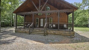 A rustic cabin with a stone foundation, a wooden deck, and a covered porch.