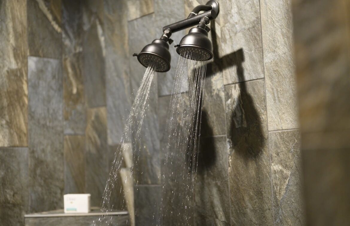 Ducha con varios cabezales, agua fluyendo y pared de piedra de fondo.