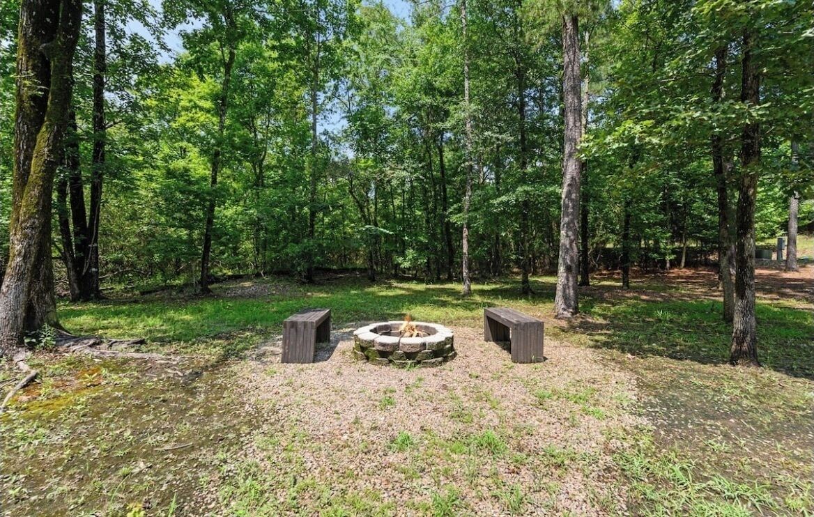 A forested area with a stone fire pit surrounded by benches.