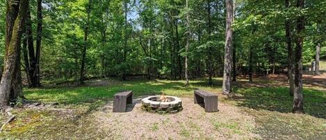 A forested area with a stone fire pit surrounded by benches.
