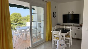 A room with a dining table, chairs, a TV, and a sliding glass door leading to an outdoor area with a table and chairs.