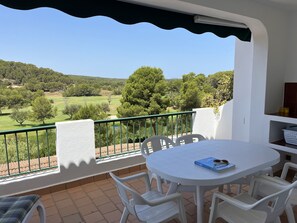 Ein Balkon mit weißem Tisch und Stühlen, der auf eine grüne Landschaft mit Bäumen und einen Golfplatz blickt.