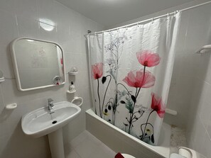 Ein Badezimmer mit einem weißen Waschbecken, einem Spiegel und einer Duschvorhang mit floralem Muster.