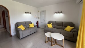 A living room with two grey sofas, each with a yellow pillow, and two small white tables with wooden legs.
