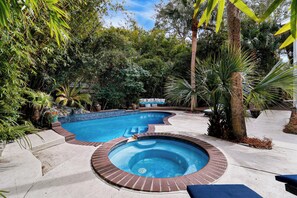 Piscina com hidromassagem, rodeada por vegetação exuberante e área de estar com sofá estampado.