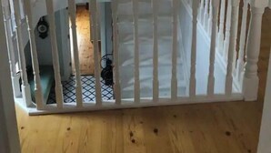 Een kamer met een houten vloer, een witte leuning en een hanglamp.