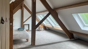 An attic bedroom with exposed wooden beams, skylights, a bed, and a chair.