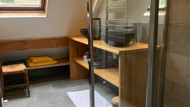 A modern bathroom with a glass shower enclosure, a wooden bench, and a sink with a black basin.