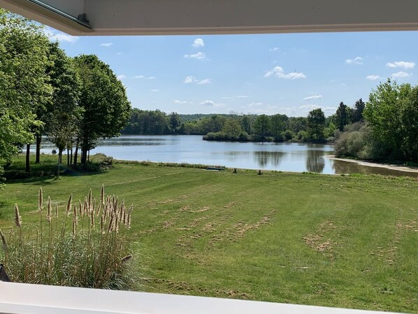 A view of a lake from a covered outdoor area with a grassy lawn and trees.