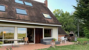 A house with a large glass door, a patio with a table and chairs, and a stone fireplace.