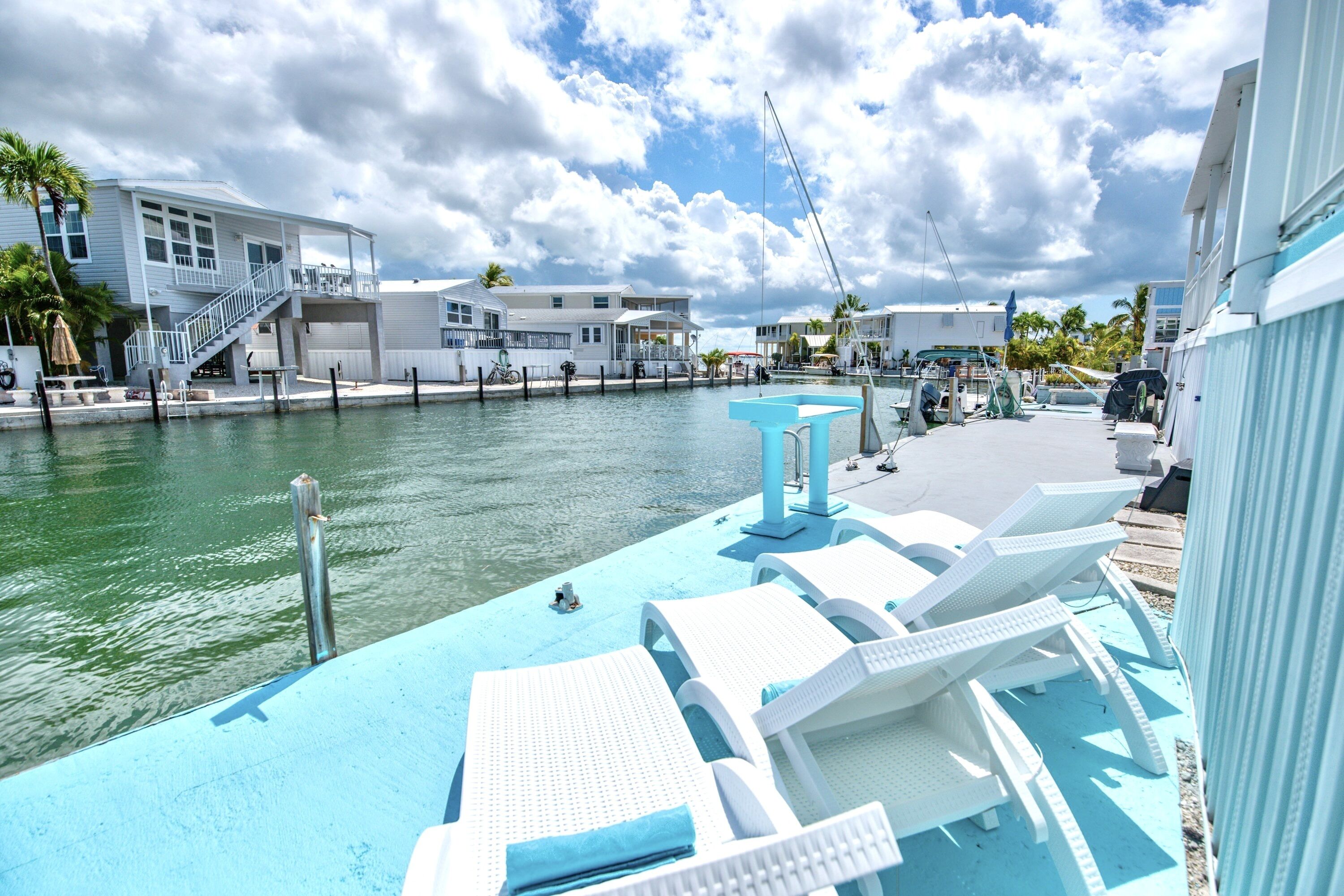 A waterfront property with a dock, lounge chairs, and a boat.
