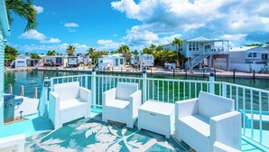Un espace aménagé au bord de la piscine, avec des meubles en osier blancs, une vue dégagée sur l’eau et une rangée de véhicules récréatifs en arrière-plan.