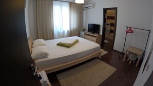 A hotel room with a bed, a TV, a small desk, a mirror, and a coat rack.