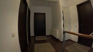A hallway with a wooden floor, a radiator, a light fixture, and a door at the end.