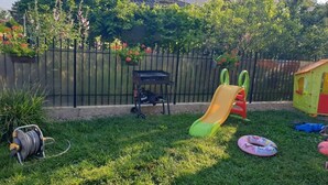 A grassy backyard with a slide, a hose reel, and a small playhouse.