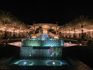 Ein Nachtbild eines Hotels mit Springbrunnen, Palmen und Lichterketten.