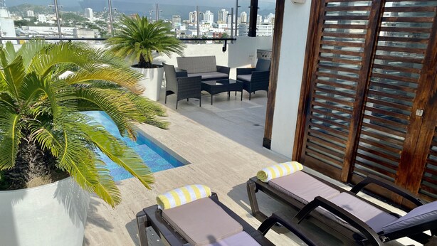 A balcony with lounge chairs, a small pool, and a city view. - Beautiful Executive Penthouse (Santa Marta)