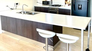 A modern kitchen with a central island, stainless steel bar stools, a built-in microwave, and a black refrigerator. - Beautiful Executive Penthouse (Santa Marta)