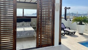 A bedroom with a bed, wooden shutters, a view of the sea, a small balcony with a pool, and a potted plant. - Beautiful Executive Penthouse (Santa Marta)