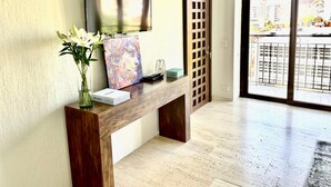 A modern living room with a wooden console table, a flat-screen TV, a vase with flowers, and a large window with a city view. - Beautiful Executive Penthouse (Santa Marta)