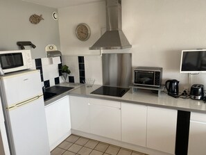Uma cozinha moderna com armários brancos, coifa de aço inoxidável, micro-ondas, forno elétrico e chaleira.
