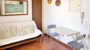 Una habitación pequeña y funcional con sofá, una mesa de comedor con dos sillas, microondas y una kitchenette.