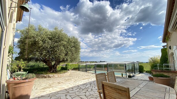 A patio with stone flooring, a table with chairs, a glass-enclosed pool, and a large tree. - Villa for 10 people with swimming pool. (Montpeyroux)