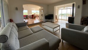 A spacious living room with a large sofa set, a flat-screen TV, and a dining area with chairs and a table. - Villa for 10 people with swimming pool. (Montpeyroux)