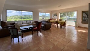 A spacious living room with a large dining table, comfortable seating, and large windows offering a view of the countryside. - Villa for 10 people with swimming pool. (Montpeyroux)