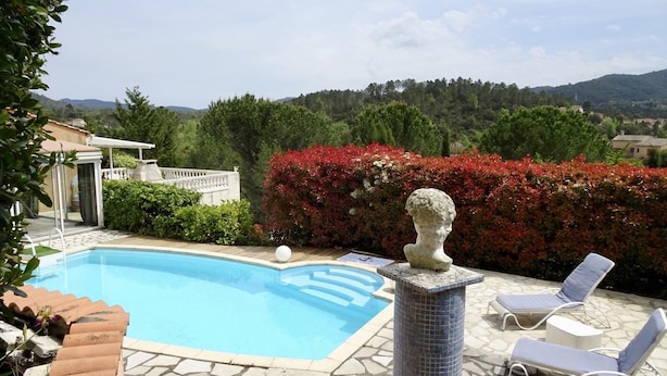 A swimming pool with a stone sculpture in the center, surrounded by a patio area with lounge chairs and a view of a forested hillside. - House with pool next to lake Saint-Cassien in the Esterel valleys. 20 min Cannes (Montauroux)