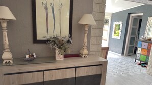 A modern interior with a wooden console table, two wall-mounted lamps, a framed abstract painting, and a colorful cabinet. - House with pool next to lake Saint-Cassien in the Esterel valleys. 20 min Cannes (Montauroux)