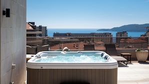 A hot tub on a balcony with a view of the sea and buildings.