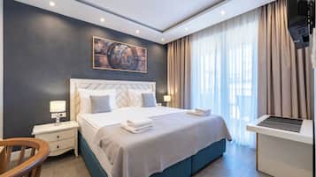 Una habitación de hotel moderna con una cama grande, mesitas de noche, un escritorio y un amplio ventanal con cortinas.