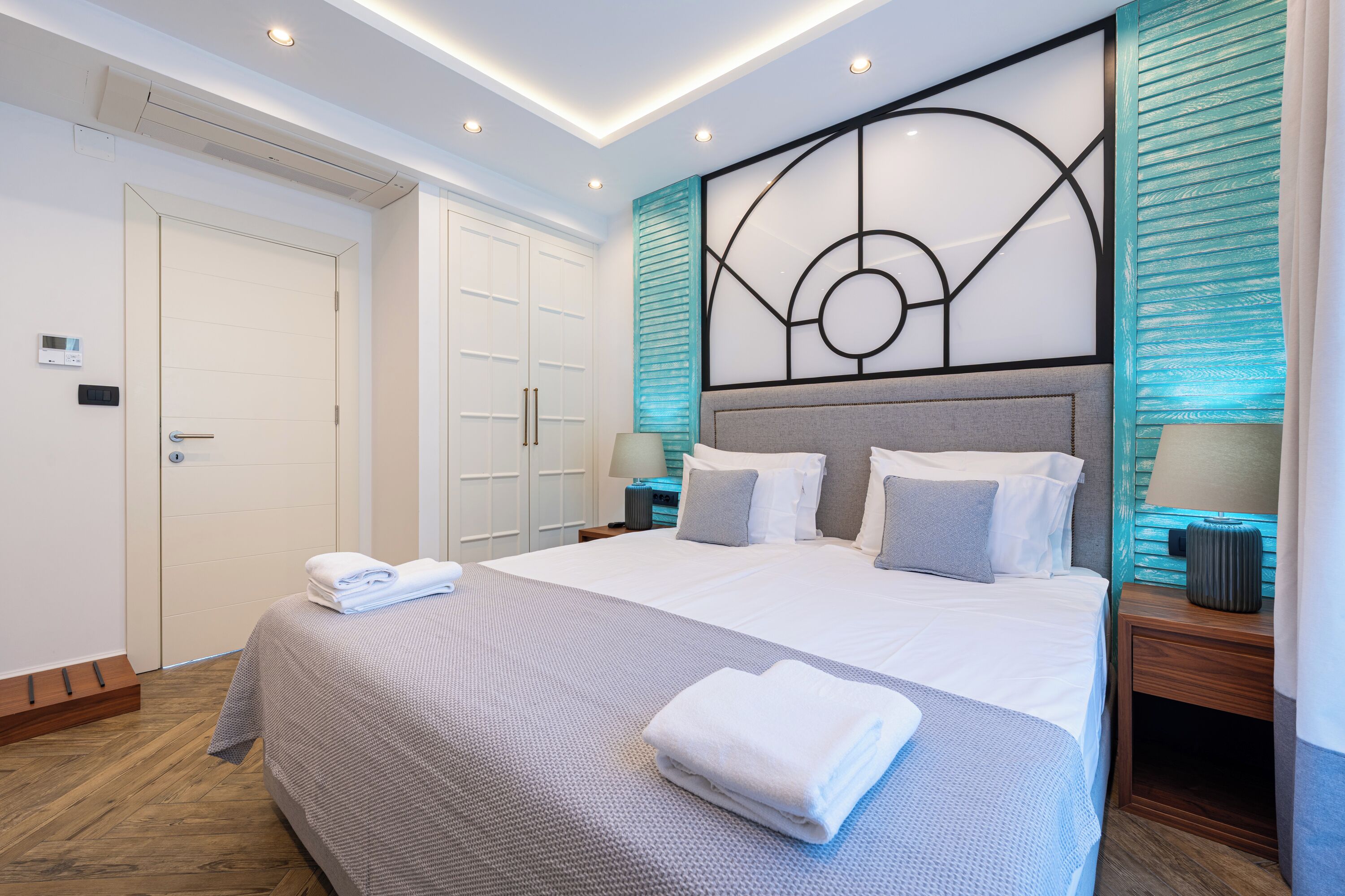 Une chambre d’hôtel moderne dotée d’un grand lit, d’une tête de lit au motif géométrique, d’un plancher en bois et d’un panneau de commande fixé au mur.