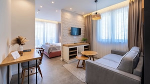 A modern living room with a sofa, a dining table, a TV mounted on a stone wall, and a large window with curtains.