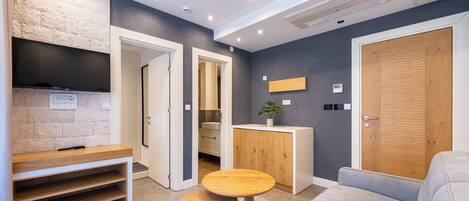 A modern room with a flat-screen TV, a wooden bench, a small table, a sofa, and a cabinet.