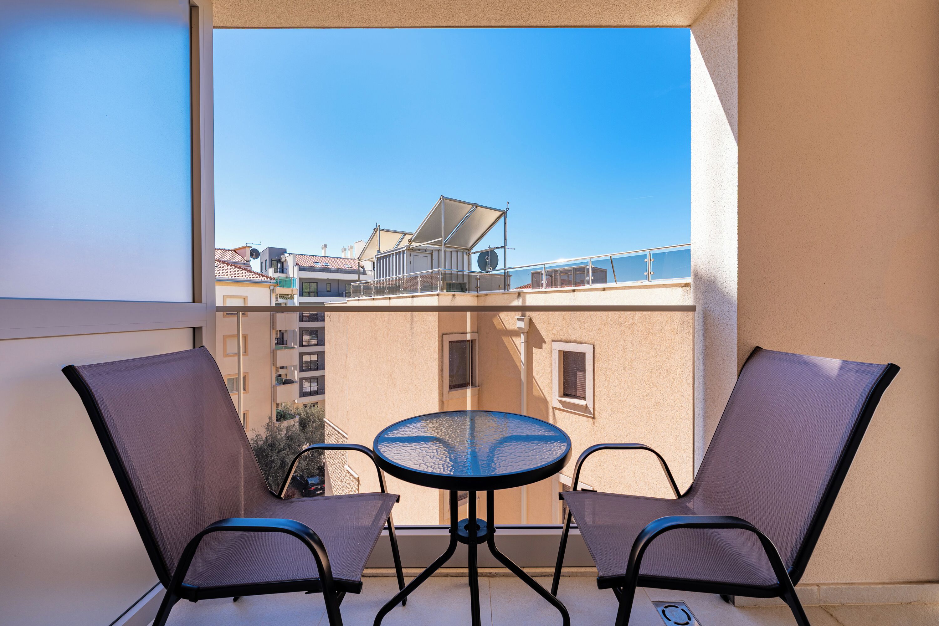 Ein Balkon mit zwei Stühlen und einem Tisch, mit Blick auf ein Gebäude mit einem Ziegeldach.
