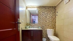 Un baño pequeño con puerta roja, un lavamanos, un inodoro y un espejo.