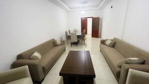 Una sala de estar con dos sofás orientados hacia una mesa de centro, una mesa de comedor con sillas, y una puerta que da a otra habitación.