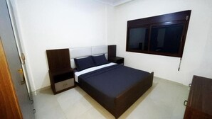 Un dormitorio con una cama, una mesita de noche, un cabecero de madera, una ventana y una puerta.