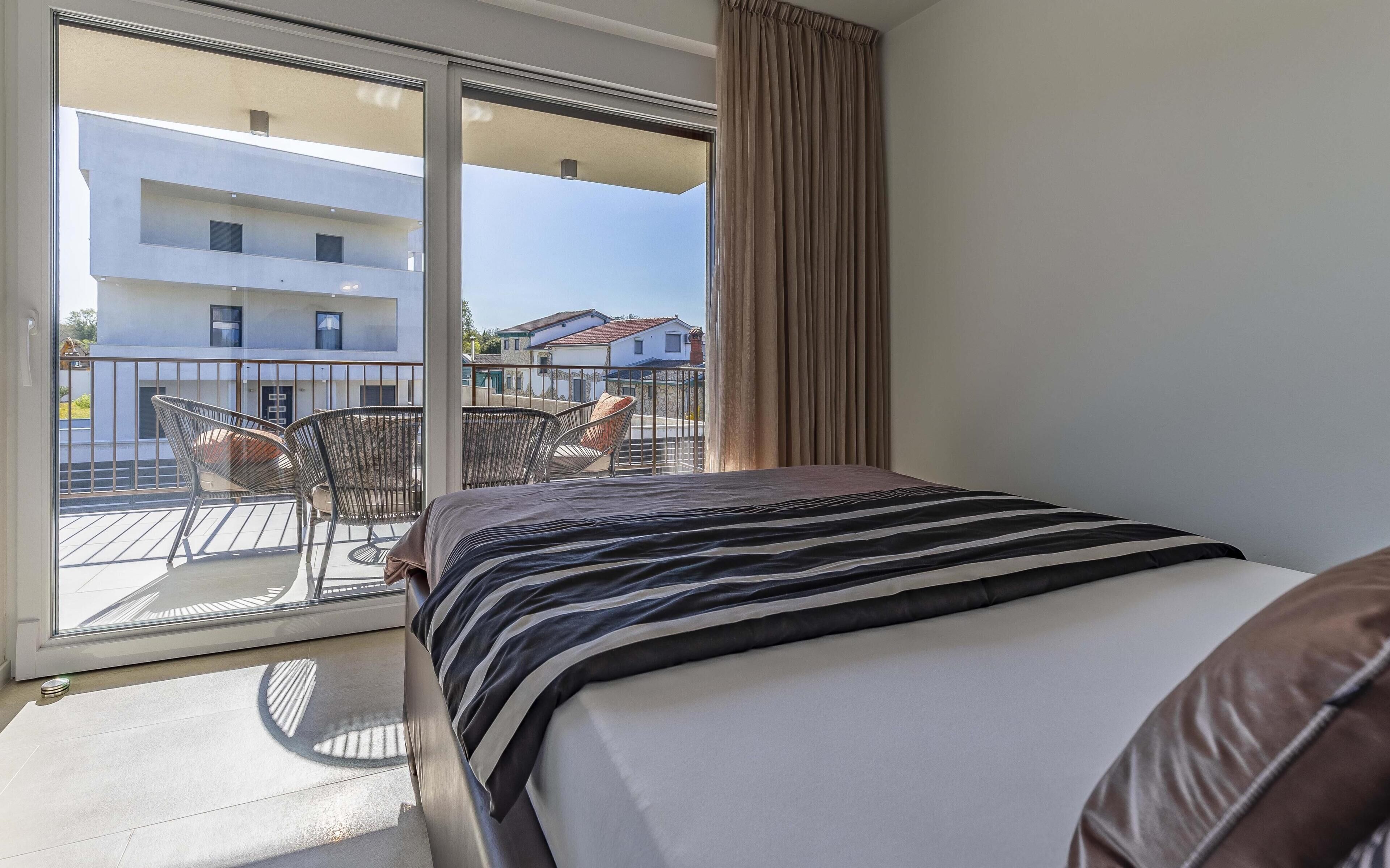 Une chambre d’hôtel avec un lit, un balcon avec des chaises et une vue sur les immeubles.