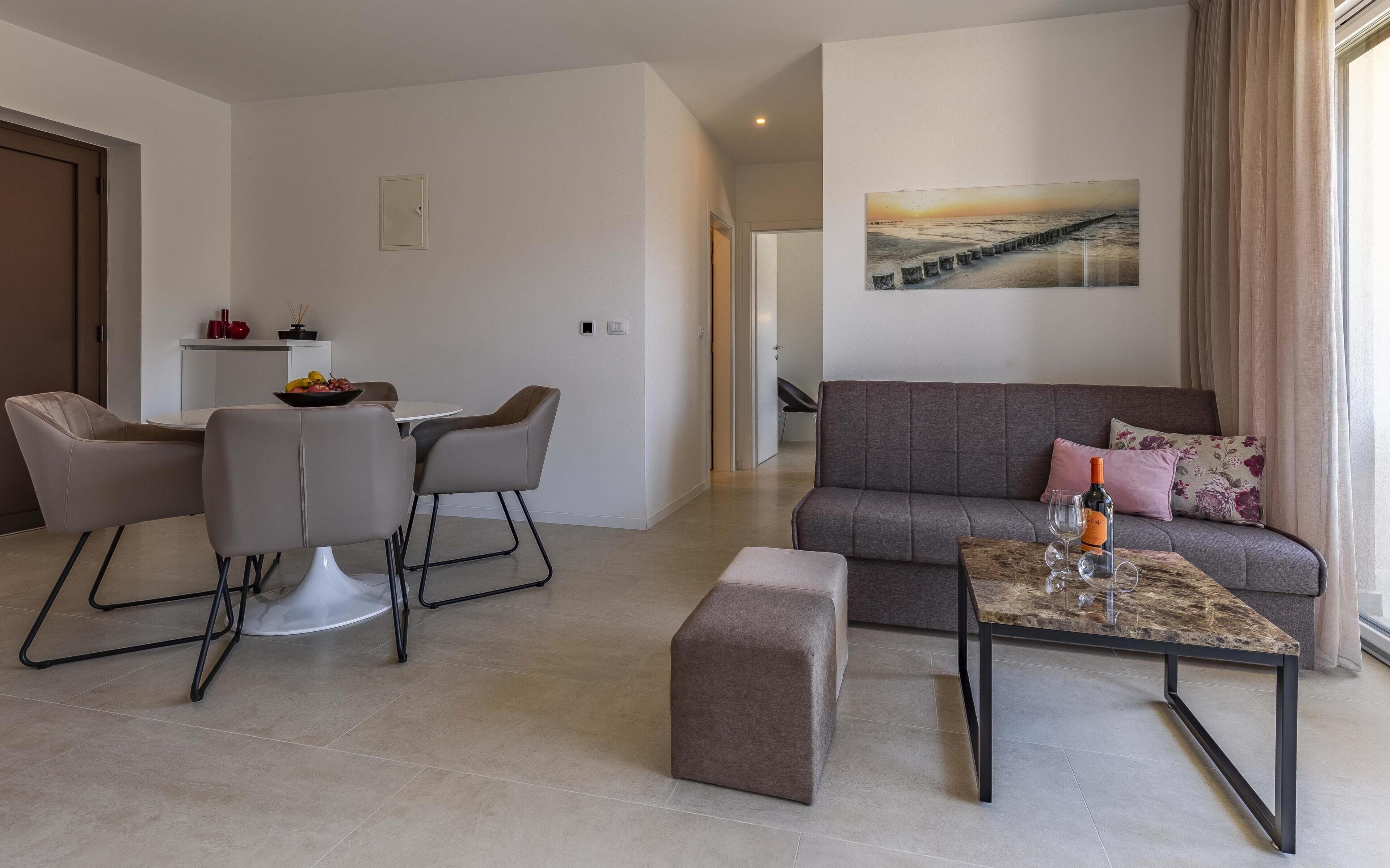 A modern living room with a grey sofa, a coffee table, and a dining area with chairs and a table.