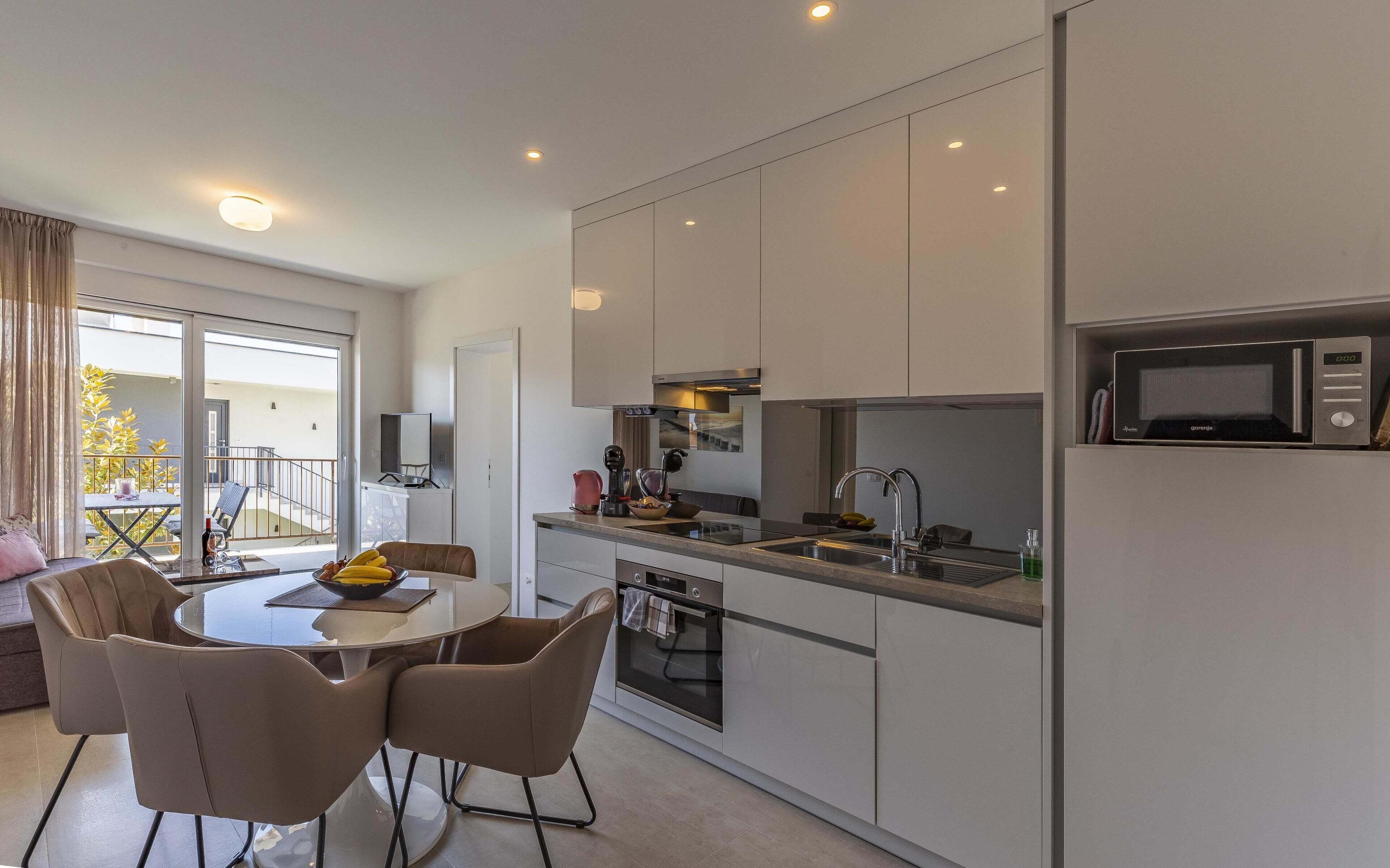 A modern kitchen with a dining area, including a round table and chairs, a built-in oven, and a microwave.