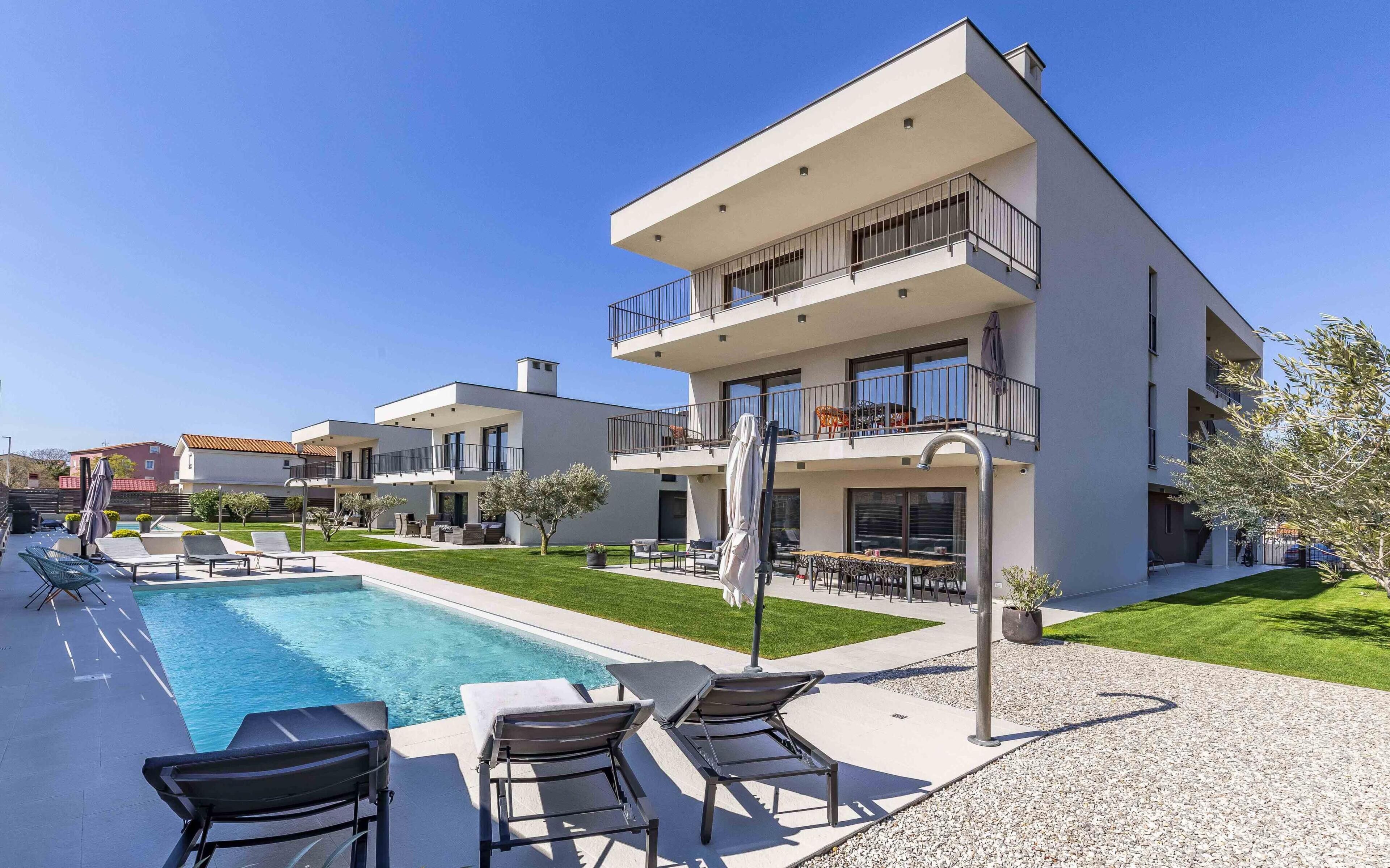 A modern multi-story building with a swimming pool, outdoor seating, and a well-maintained lawn.