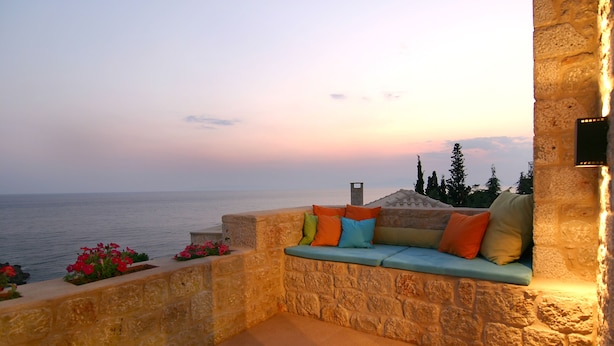 A stone-walled outdoor seating area with colorful cushions, overlooking a body of water. - Enjoy the seaside living in a centraly located, pretty sea view house (Stoupa)