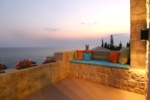 A stone-walled outdoor seating area with colorful cushions, overlooking a body of water. - Enjoy the seaside living in a centraly located, pretty sea view house (Stoupa)