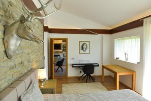 Un dormitorio con cama, escritorio, silla, lámpara, un cuadro en la pared y una cabeza de venado decorativa.
