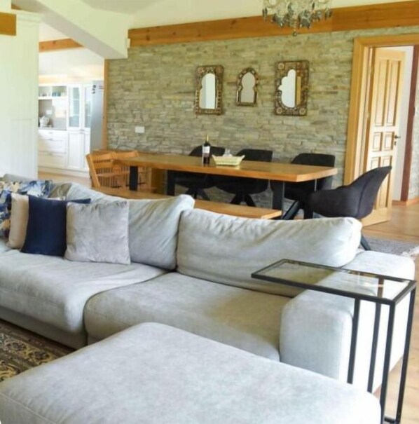 Una sala de estar moderna con un sofá seccional gris, una mesa de centro de vidrio y un comedor con una mesa y sillas de madera.